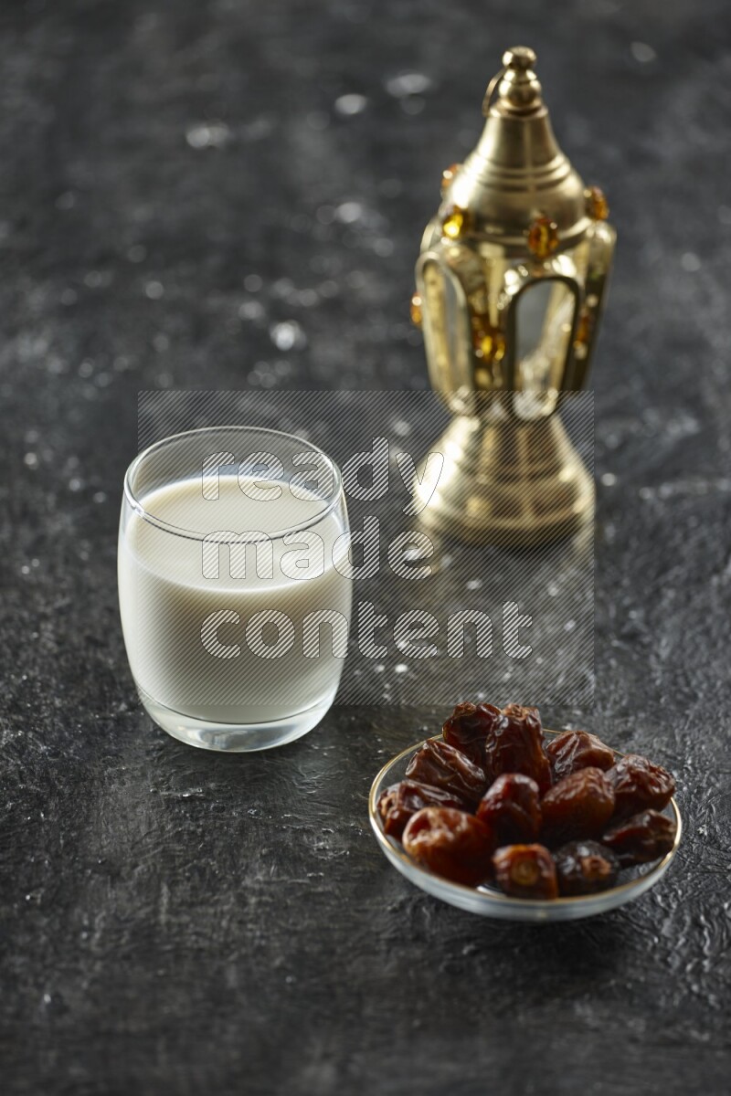 A golden lantern with different drinks, dates, nuts, prayer beads and quran on textured black background