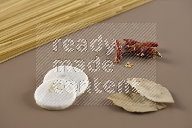 Raw pasta with different ingredients such as cherry tomatoes, garlic, onions, red chilis, black pepper, white pepper, bay laurel leaves, rosemary and cardamom on beige background