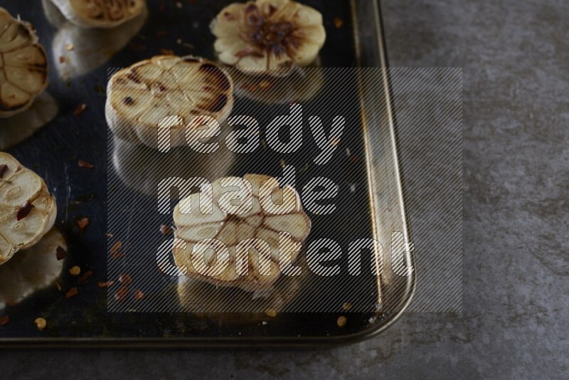 half's roasted garlic in a stainless tray on a grey textured countertop