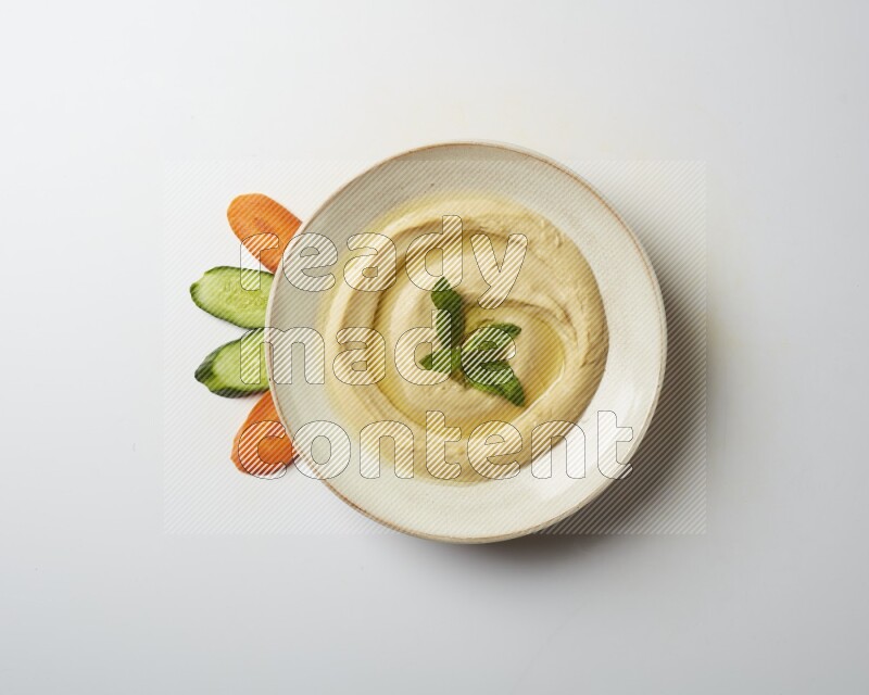 Hummus in a pottry plate garnished with mint  on a white background