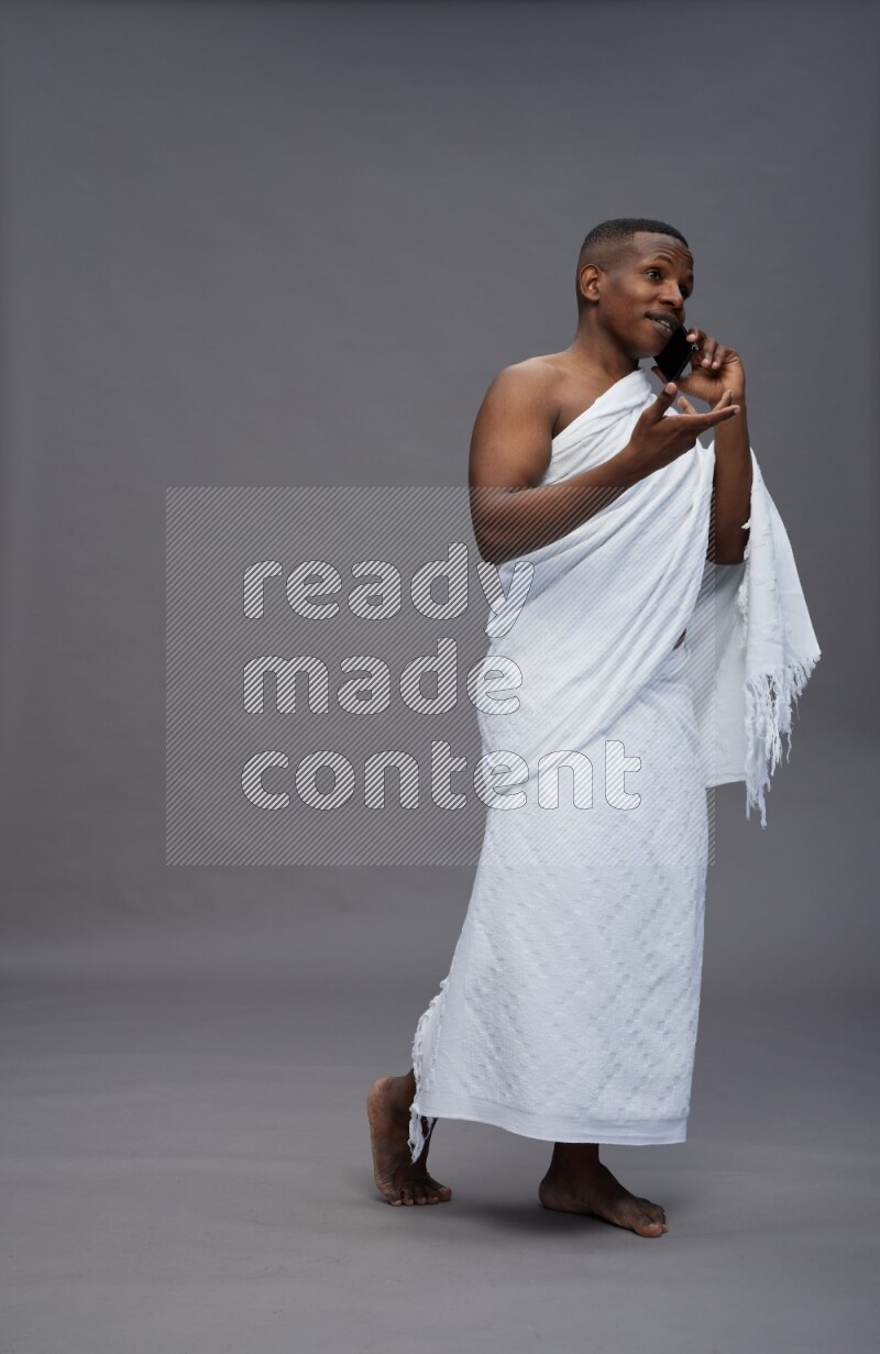 A man wearing Ehram Standing talking on phone on gray background