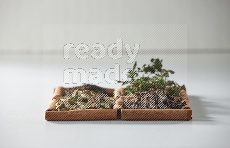 4 مربعات من أعواد القرفة ممتلئة بالشاي والهيل والنعناع والقرنفل على أرضية بيضاء