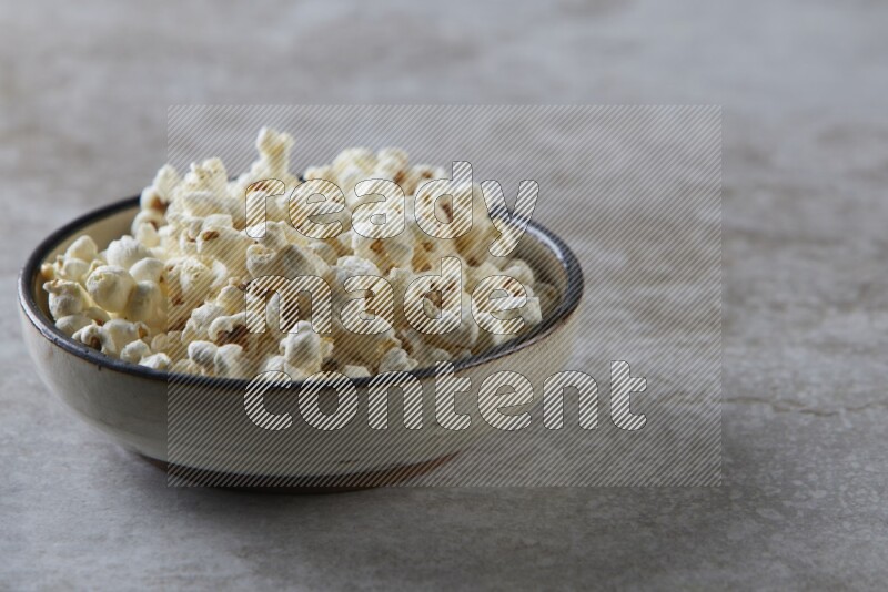 popcorn in a multi-colored pottery bowl on a grey textured countertop