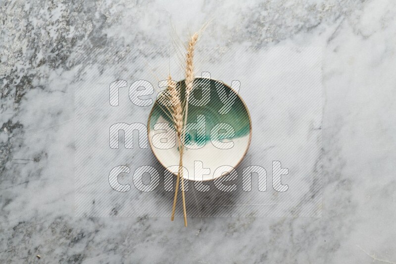 Wheat stalks on multicolored pottery plate on grey marble background