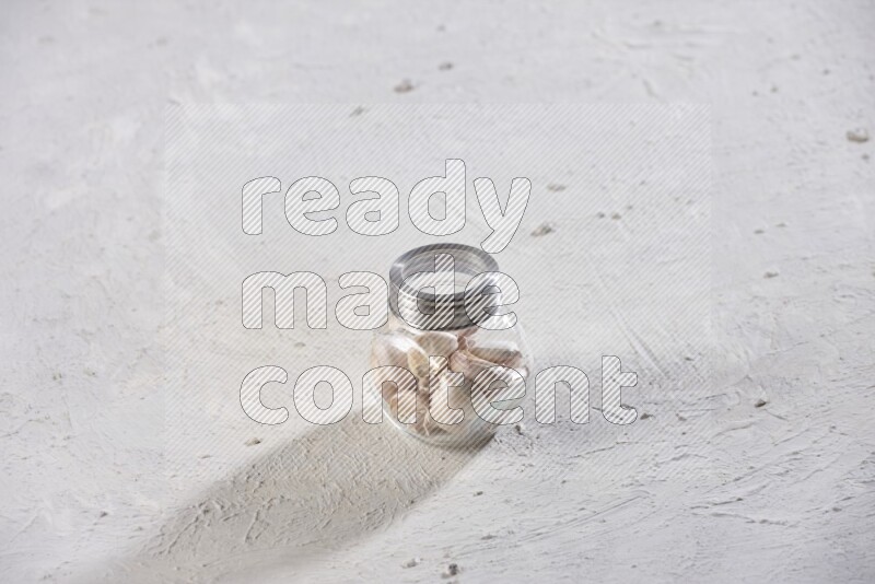 A glass spice jar full of garlic cloves on a textured white flooring