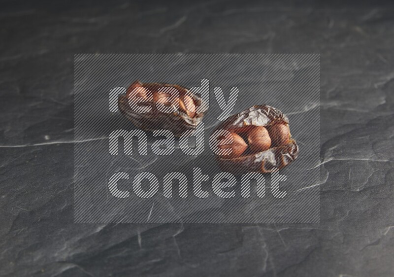two hazelnuts stuffed madjoul dates on a black textured background