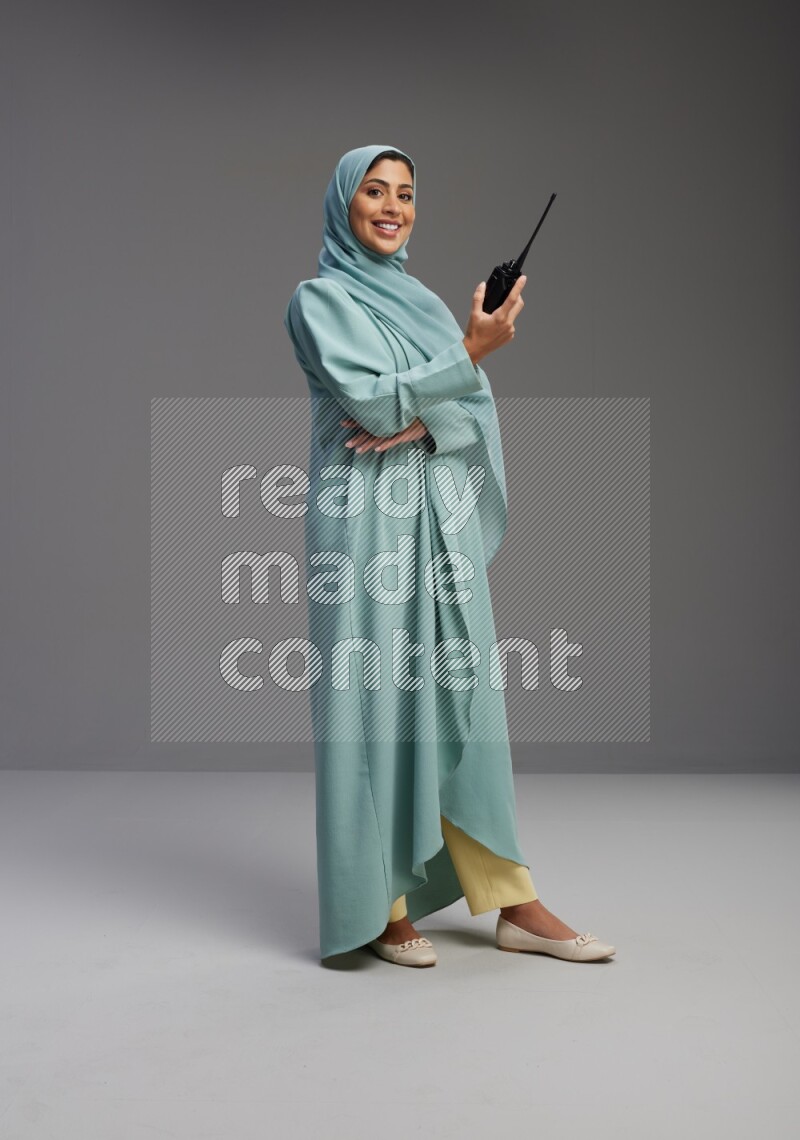 Saudi Woman wearing Abaya standing holding walkie-talkie on Gray background