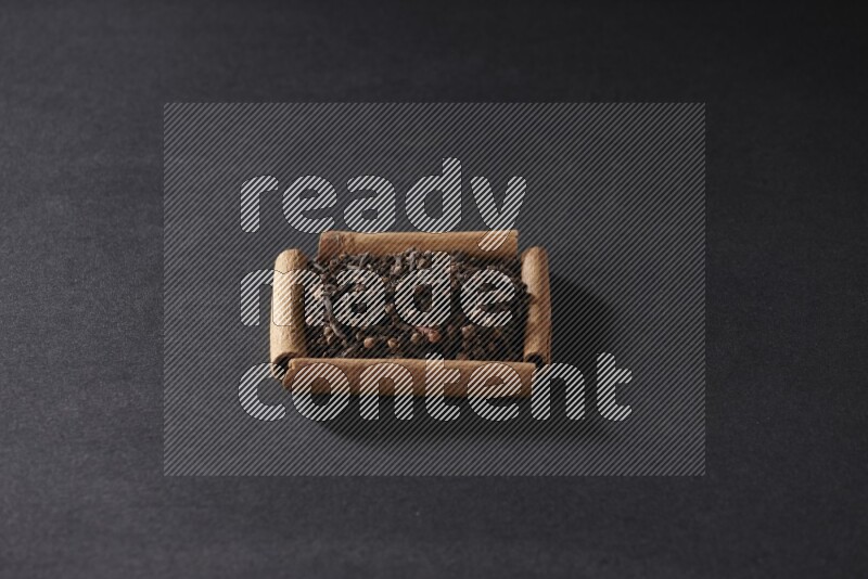 A single square of cinnamon sticks full of cloves on black flooring