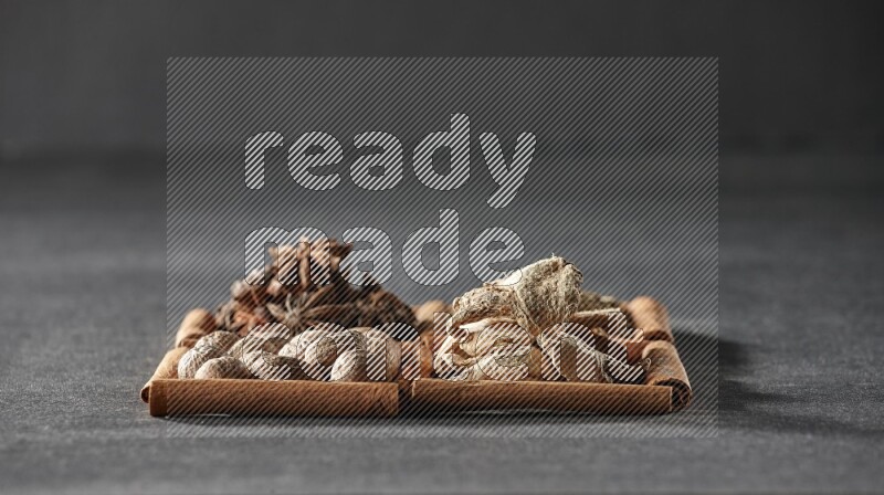 4 مربعات من عيدان القرفة ممتلئة باليانسون النجمي والكمون والزنجبيل المجفف وجوزة الطيب على أرضية سوداء