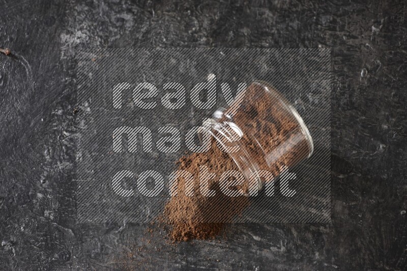 A flipped glass jar full of cloves powder on a textured black flooring