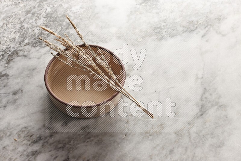 Wheat stalks on beige pottery oven bowl on grey marble background