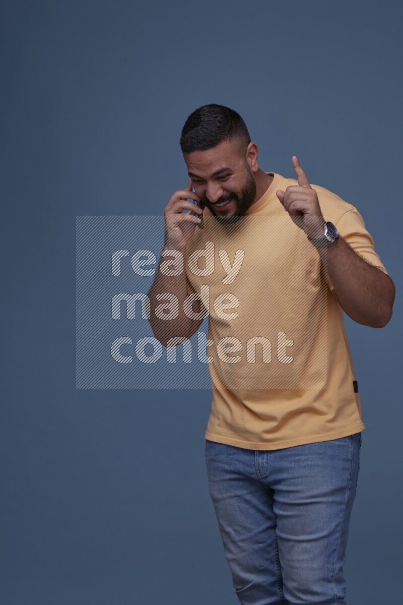 رجل يرتدي بنطال ازرق جينز وقميص اصفر بأكمام قصيره يتحدث بجواله