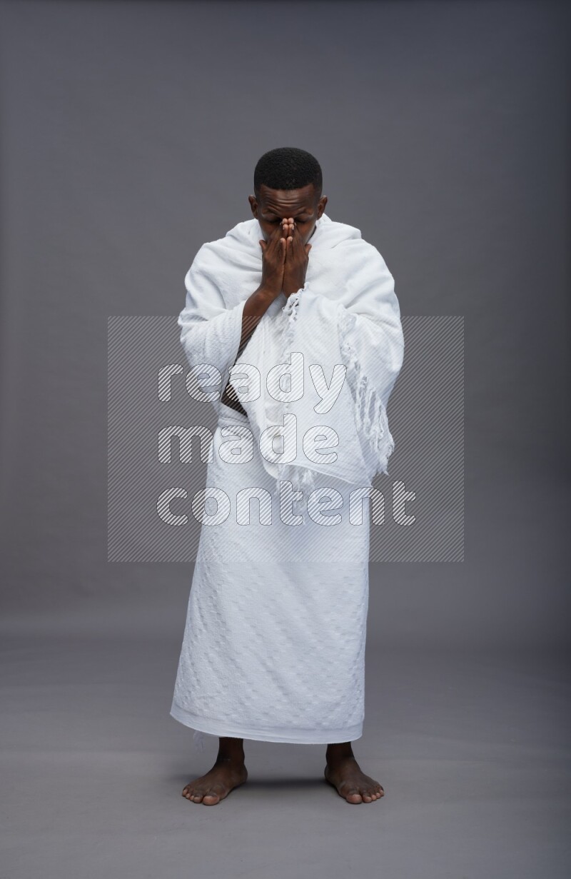 A man wearing Ehram standing showing how to sneeze on gray background
