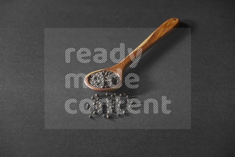 A wooden ladle full of black pepper beads on a black flooring