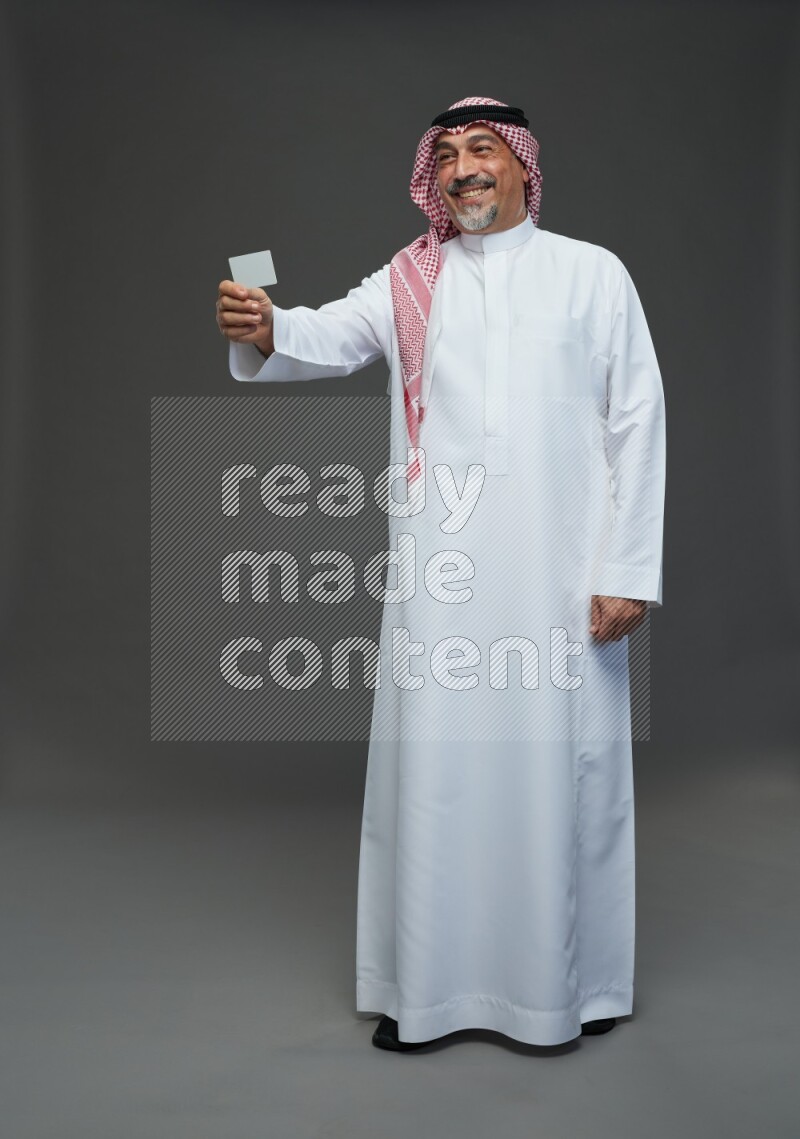 Saudi man with shomag Standing holding ATM card on gray background