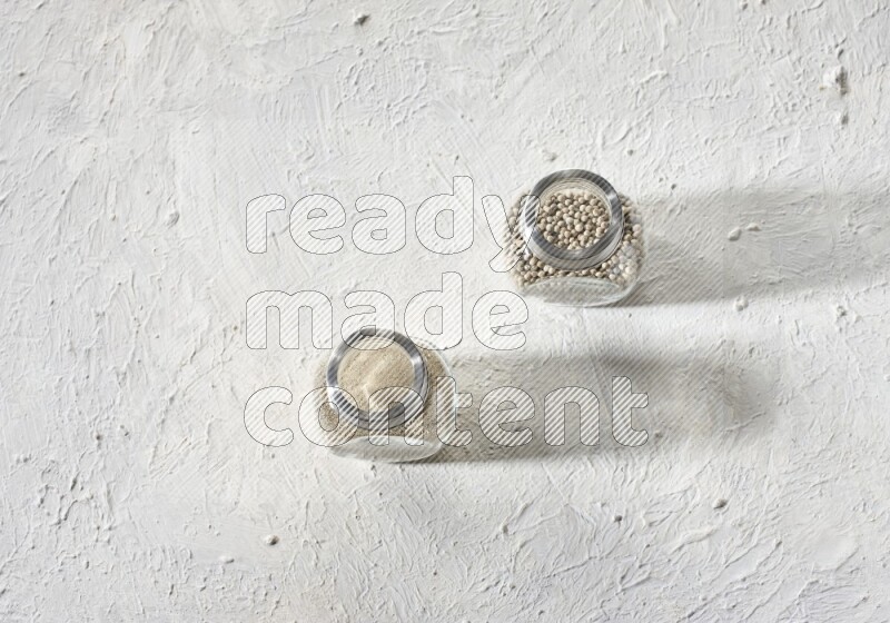 2 Herbal Glass jar full of white pepper beads and powder on textured white flooring