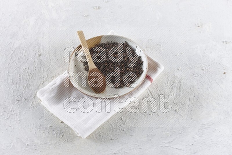 A Pottery plate full of whole cloves and a wooden spoon full of cloves powder in it on a textured white background
