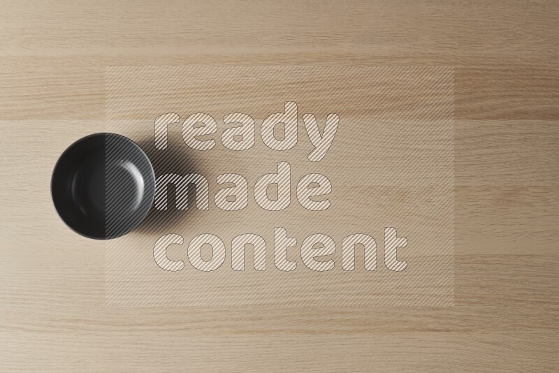 A black ceramic bowl on light wooden background