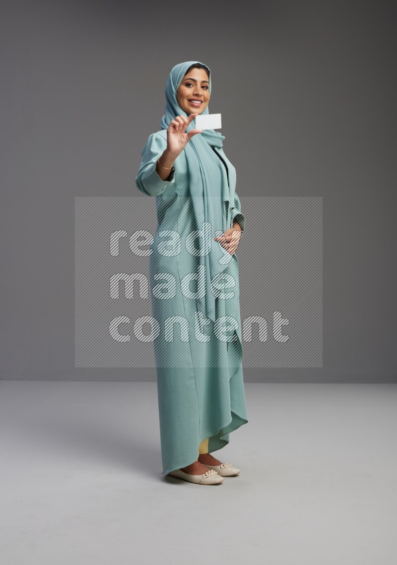 Saudi Woman wearing Abaya standing holding ATM card on Gray background