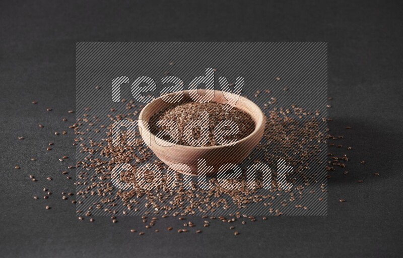 A wooden bowl full of flax surrounded by the seeds on a black flooring in different angles