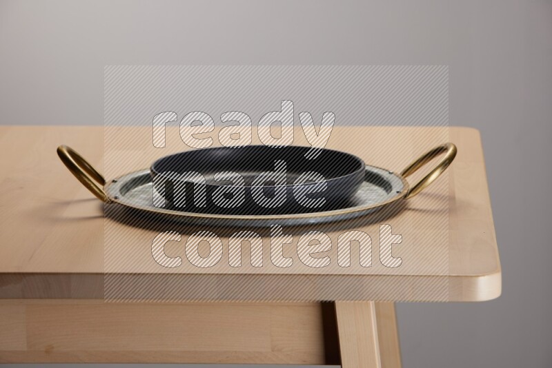 black plate placed on a rounded stainless steel metal tray with golden handels on the edge of wooden table