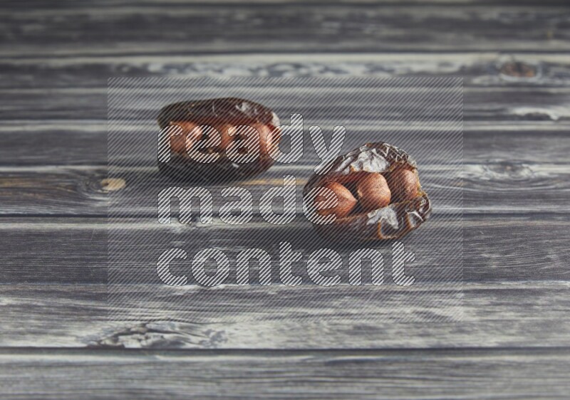 two hazelnut stuffed madjoul dates on a wooden grey background